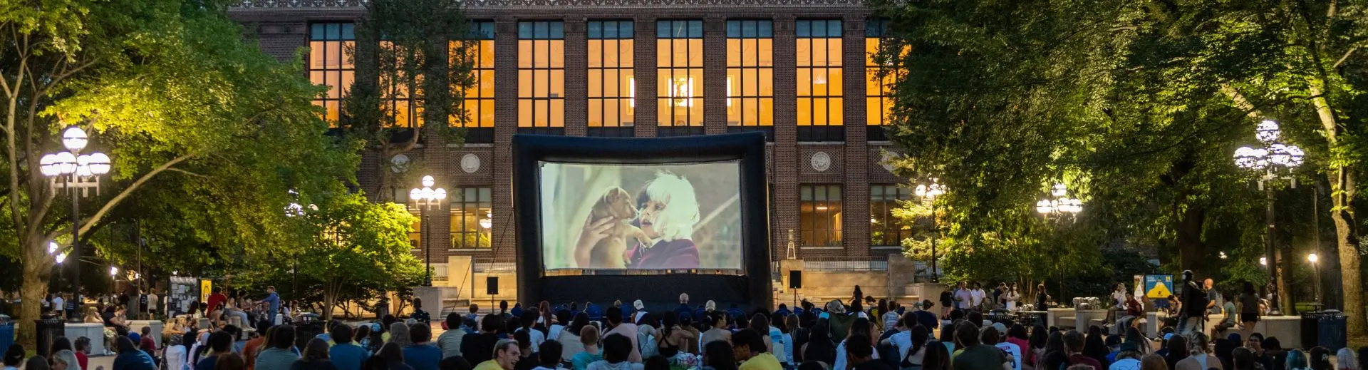 People sitting on the ground watching a movie shown on the Diag