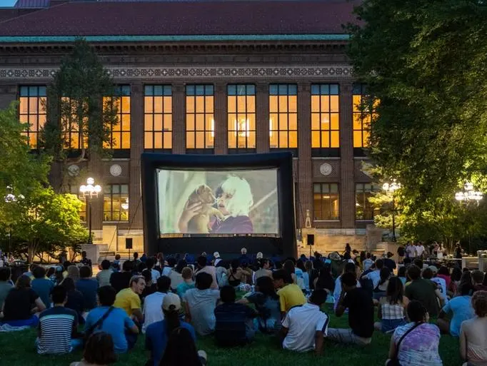 People sitting on the ground watching a movie shown on the Diag