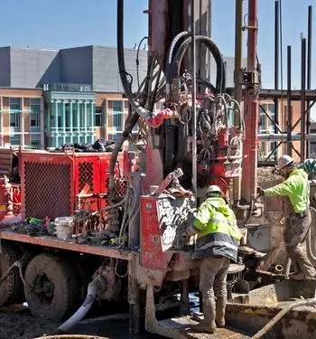 Workers with a truck and equipment in a muddy field on North Campus