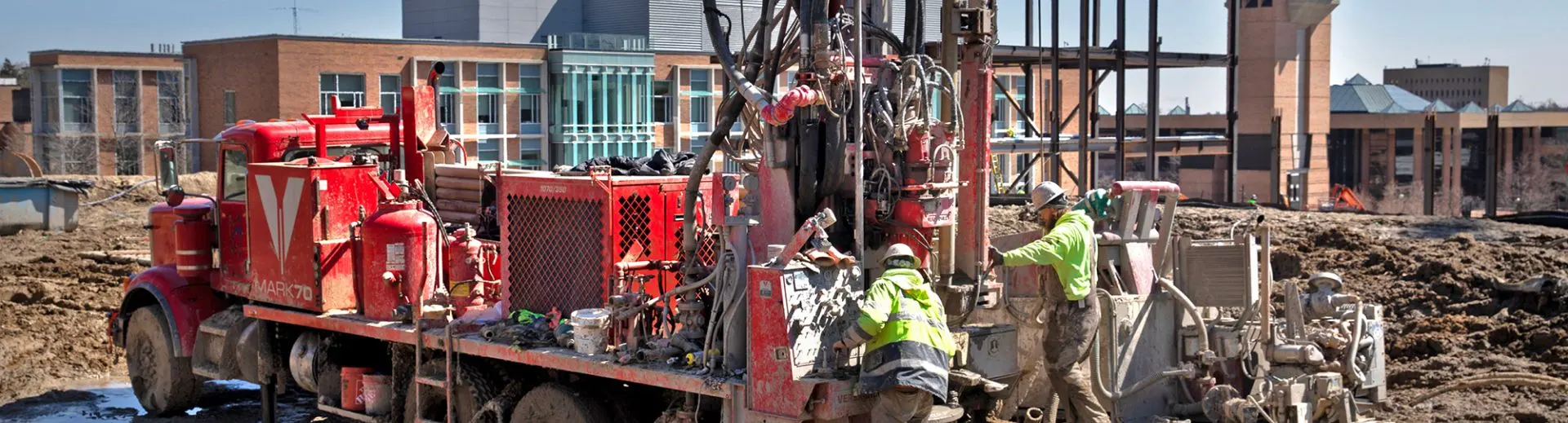 Workers with a truck and equipment in a muddy field on North Campus