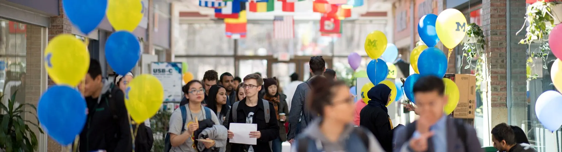 Students walking through Pierpont Commons with flags overhead and blue and yellow balloons